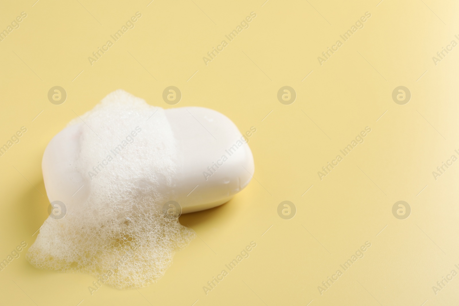 Photo of Soap with fluffy foam on yellow background, space for text