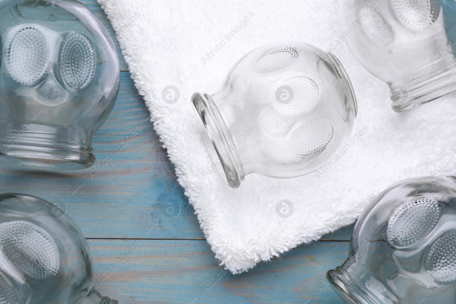 Photo of Glass cups and towel on light blue wooden table, flat lay. Cupping therapy