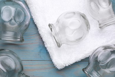 Glass cups and towel on light blue wooden table, flat lay. Cupping therapy