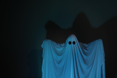 Photo of Creepy ghost. Woman covered with sheet on dark background, space for text