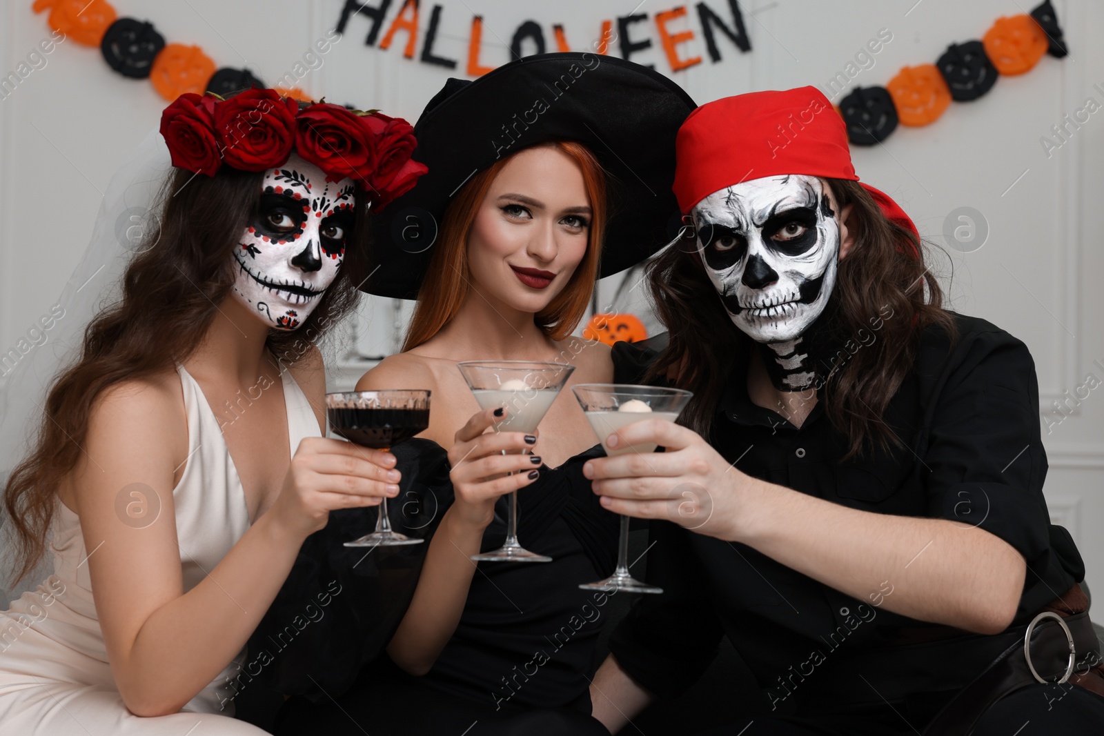 Photo of Group of people in scary costumes with cocktails celebrating Halloween indoors