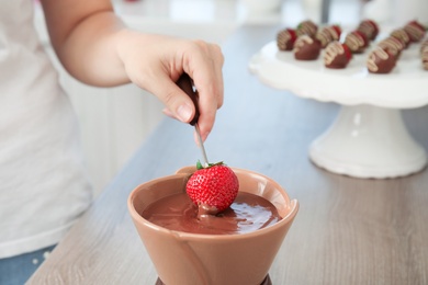 Woman dipping ripe strawberry into bowl with chocolate fondue, closeup