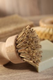 Photo of Cleaning brush and soap bar on wooden table, closeup