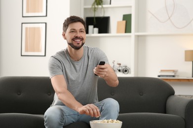 Happy man changing TV channels with remote control on sofa at home
