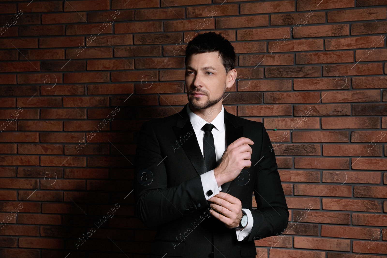 Photo of Man wearing stylish suit and cufflinks near brick wall