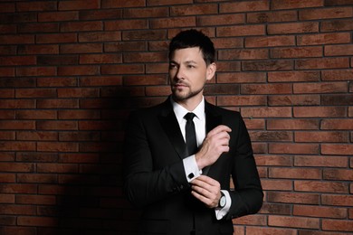 Photo of Man wearing stylish suit and cufflinks near brick wall