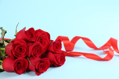 Photo of Beautiful red roses and ribbons on light blue background, space for text. St. Valentine's day celebration