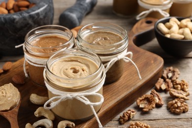 Tasty nut butters and raw nuts on wooden table, closeup