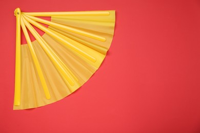 Photo of Bright yellow hand fan on red background, top view. Space for text