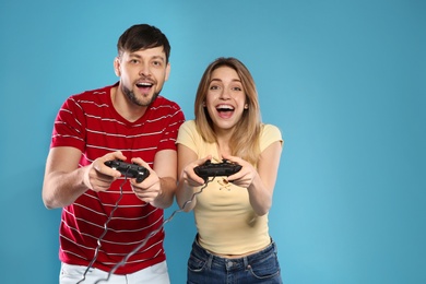 Emotional couple playing video games with controllers on color background