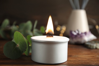 Photo of Burning candle and eucalyptus on wooden table, closeup