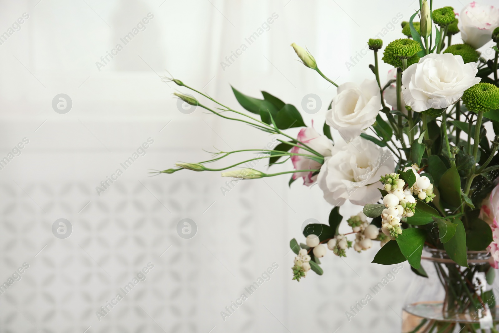 Photo of Glass vase with bouquet of beautiful flowers on blurred background. Space for text