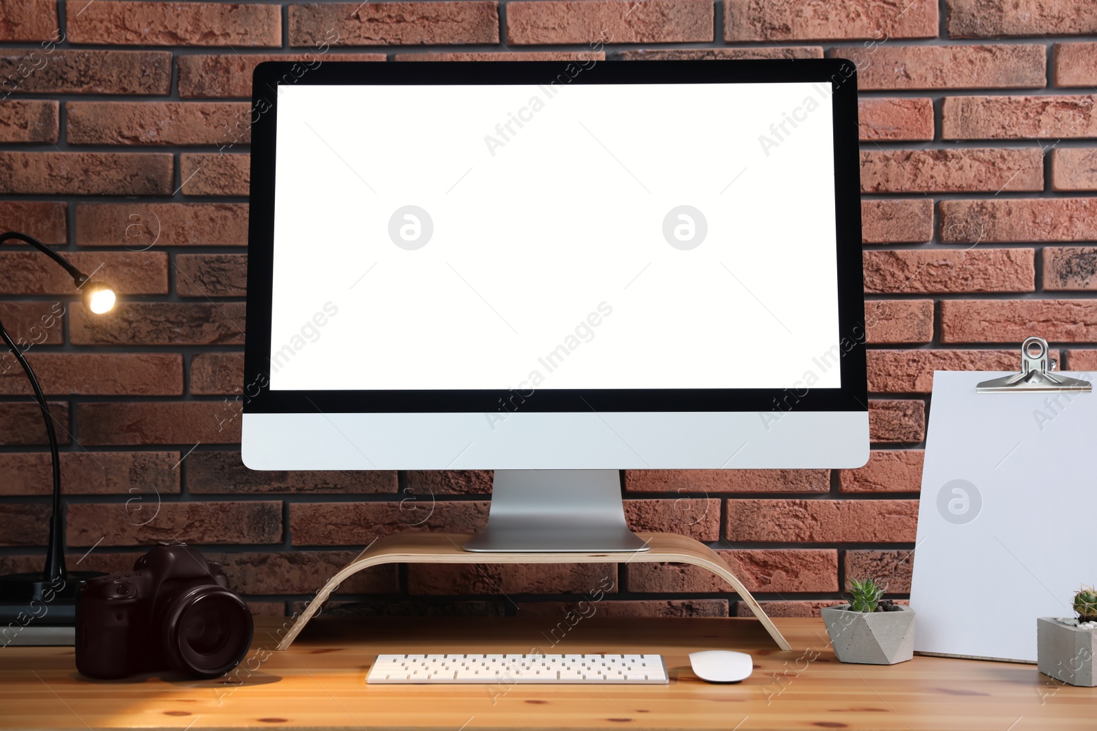 Photo of Comfortable workplace with modern computer on wooden table near brick wall. Space for text