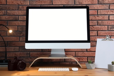 Comfortable workplace with modern computer on wooden table near brick wall. Space for text