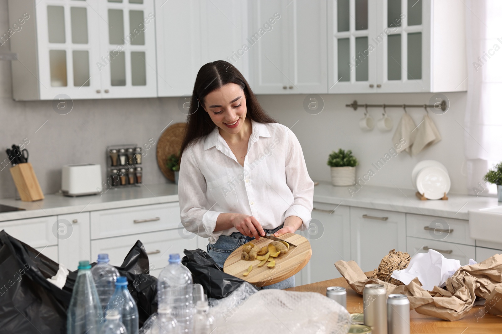 Photo of Garbage sorting. Woman putting food waste into plastic bag at table in kitchen