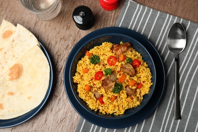 Photo of Flat lay composition with plate of rice pilaf and meat on wooden background