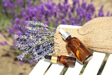 Bottles of essential oil and lavender flowers on white wooden table in field, closeup