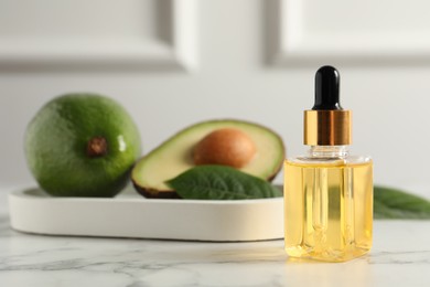 Photo of Bottle of essential oil and avocados on white marble table, space for text