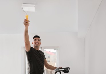 Photo of Man painting ceiling with roller in room. Space for text