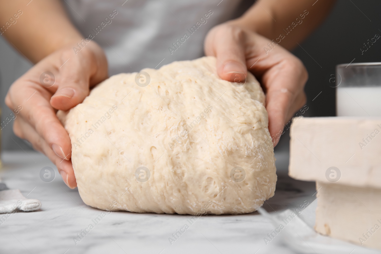 Photo of Woman kneading dough at white marble table, closeup