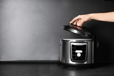 Young woman using modern multi cooker on table, space for text