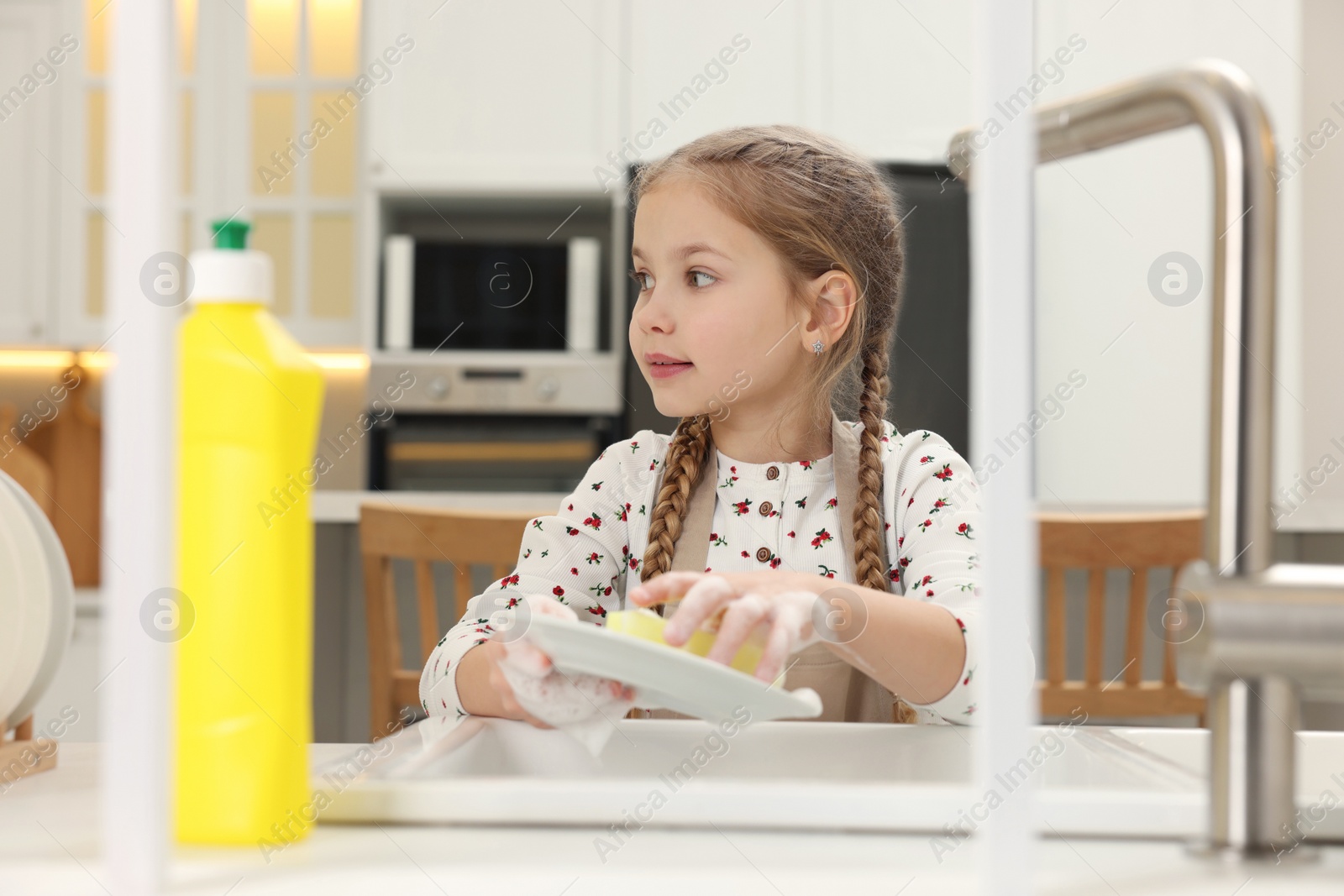 Photo of Little girl washing plate above sink in kitchen