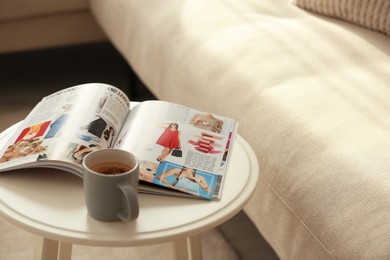 Photo of Fashion magazine and cup of hot drink on white table in living room