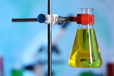 Photo of Flask with yellow liquid on retort stand in laboratory, closeup