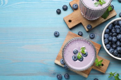 Photo of Glasses of blueberry smoothie with mint and fresh berries on light blue wooden table, flat lay. Space for text
