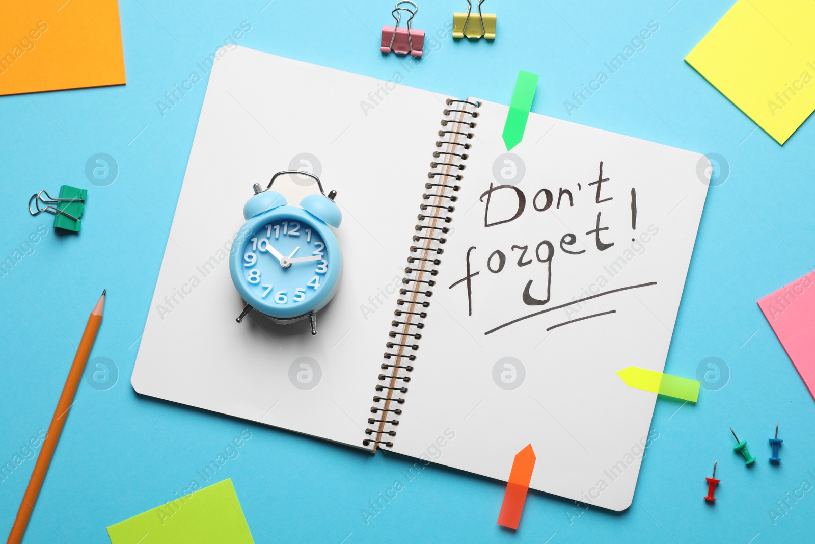 Photo of Alarm clock, stationery and notebook with phrase Don't forget on light blue background, flat lay. Reminder concept