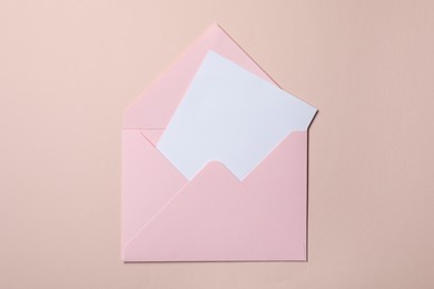 Letter envelope with card on beige background, top view