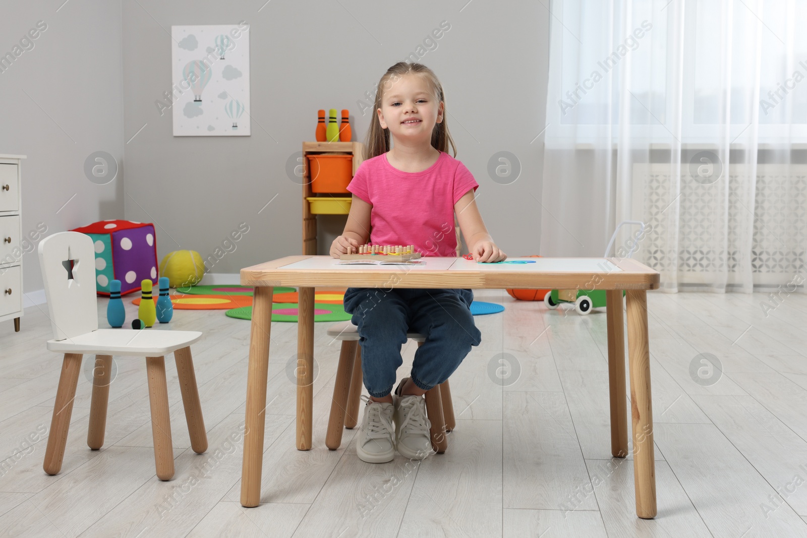 Photo of Motor skills development. Happy girl with geoboard and rubber bands at white table in kindergarten