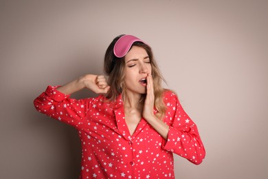 Photo of Young tired woman with sleeping mask yawning on beige background