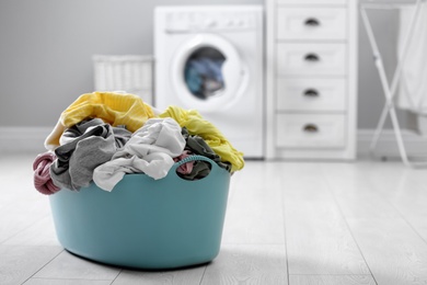 Photo of Plastic basket with dirty laundry on floor indoors, space for text