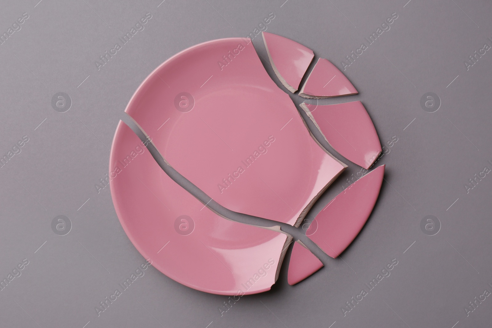 Photo of Pieces of broken pink ceramic plate on grey background, top view