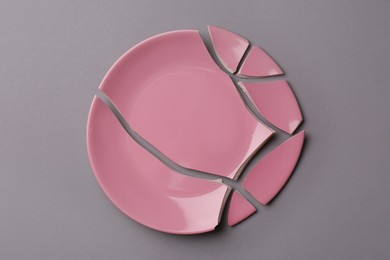 Pieces of broken pink ceramic plate on grey background, top view