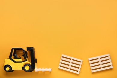 Photo of Toy forklift and wooden pallets on orange background, flat lay. Space for text