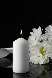 Photo of Burning candle, white chrysanthemum flowers and ribbon on black mirror surface in darkness, closeup with space for text. Funeral symbols