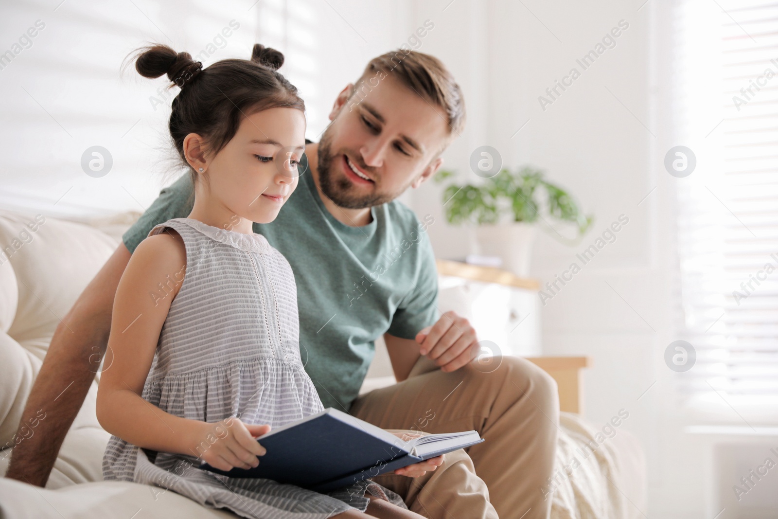 Photo of Little girl with father reading fairy tale in living room