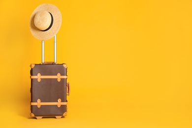 Photo of Vintage travel suitcase with hat on yellow background, space for text. Summer vacation
