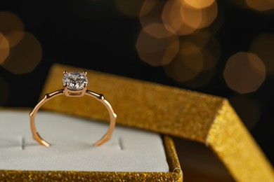 Beautiful engagement ring in box against blurred festive lights, closeup. Space for text