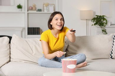 Photo of Happy woman eating popcorn while watching TV on sofa at home