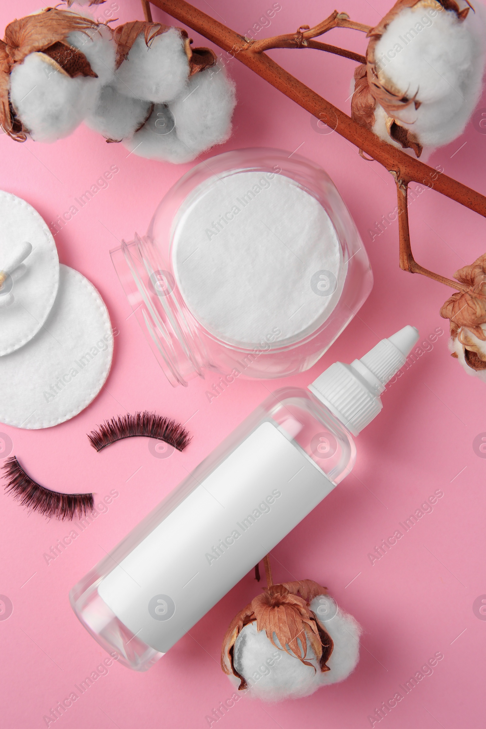 Photo of Bottle of makeup remover, cotton flowers, pads and false eyelashes on pink background, flat lay