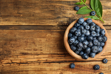 Fresh ripe blueberries in bowl on wooden table, flat lay. Space for text