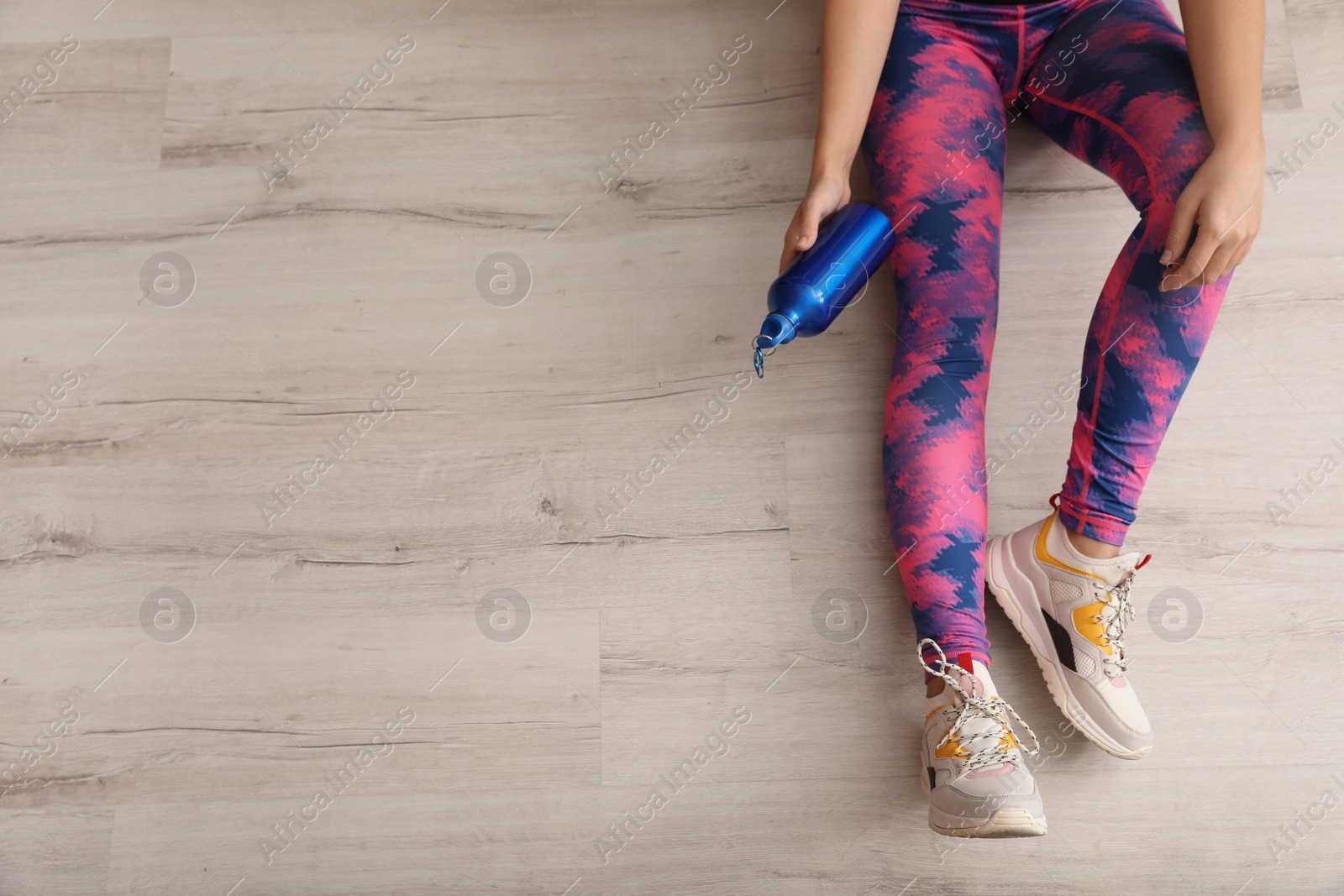 Photo of Woman in sportswear with bottle of water sitting on floor indoors, top view. Space for text