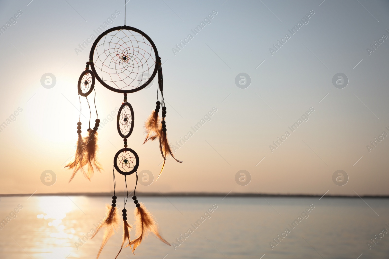 Photo of Beautiful handmade dream catcher near river at sunset. Space for text