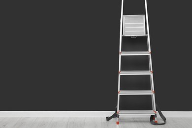 Photo of Metallic folding ladder near light gray wall indoors, space for text
