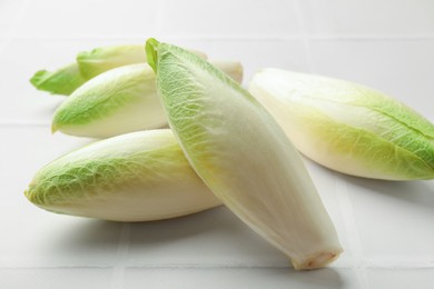 Photo of Fresh raw Belgian endives (chicory) on white tiled table, closeup