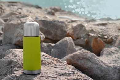 Photo of Metallic thermos with hot drink on stone near sea, space for text