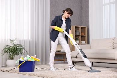 Happy young housewife vacuuming carpet at home